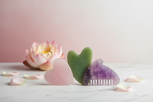 Trois Gua Sha en pierre naturelle — quartz rose, jade vert et améthyste violette — posés sur marbre blanc avec fleur de lotus, fond zen pastel