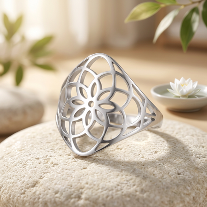 Bague fleur de vie argentée en gros plan sur une pierre beige, avec un lotus blanc en arrière-plan