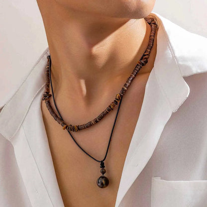 Collier perle bois homme en superposition avec un cordon noir à pendentif rond, vue de face sur le torse.