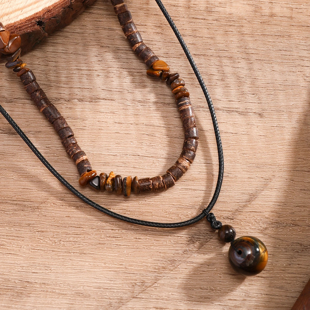 Collier perle bois homme posé sur du bois clair, détail des perles brunes et du pendentif rond sur cordon noir.