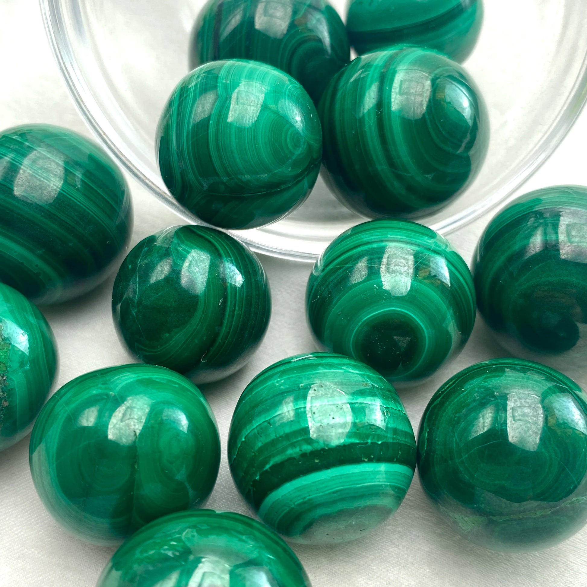 Sphères de malachite sortant d'un bol en verre, pierre naturelle de guérison aux reflets verts hypnotiques