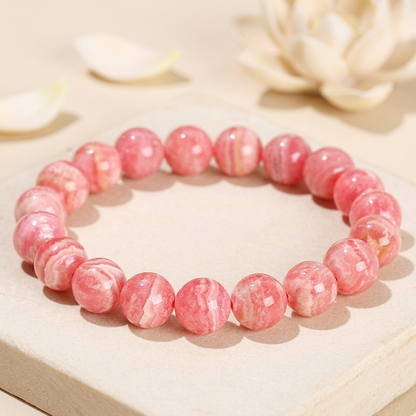 bracelet énergétique femme en rhodochrosite rose à veinures blanches, posé sur une pierre claire avec un lotus en arrière-plan.