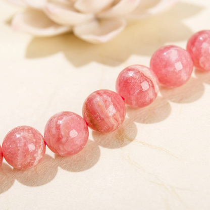 bracelet énergétique femme, détail des perles rondes de rhodochrosite rose et de leurs veinures naturelles blanches.