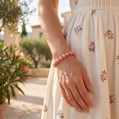 bracelet énergétique femme en rhodochrosite rose porté avec une robe claire fleurie sur une terrasse ensoleillée.