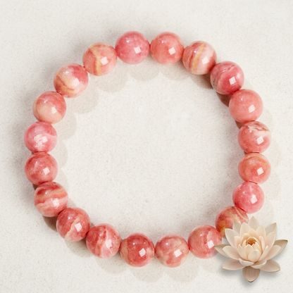 bracelet énergétique femme en rhodochrosite rose disposé en cercle sur un fond clair, près d’une fleur de lotus.