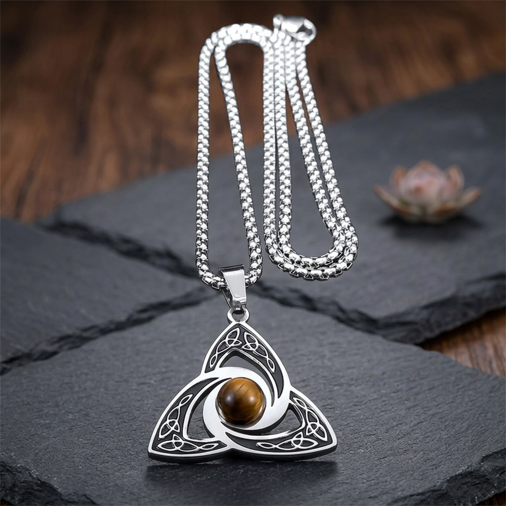 Collier oeil de tigre homme posé sur une ardoise, avec pendentif celtique et fleur de lotus en arrière-plan.