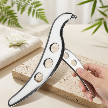 Gua sha metal argenté posé sur un galet, avec une serviette et un lotus blanc dans un décor spa.