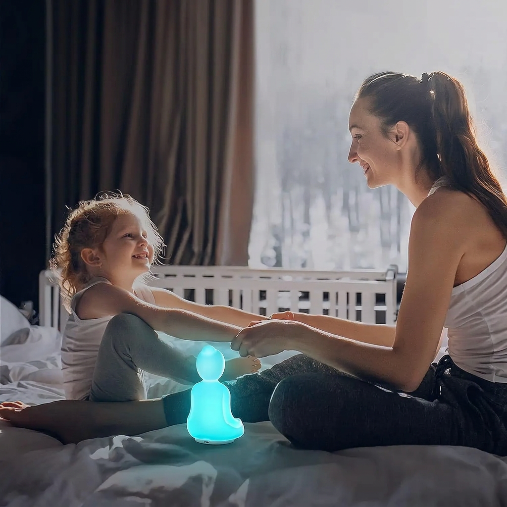 Femme et petite fille se tenant les mains sur un lit, près d’une lampe Bouddha à lumière relaxation turquoise.