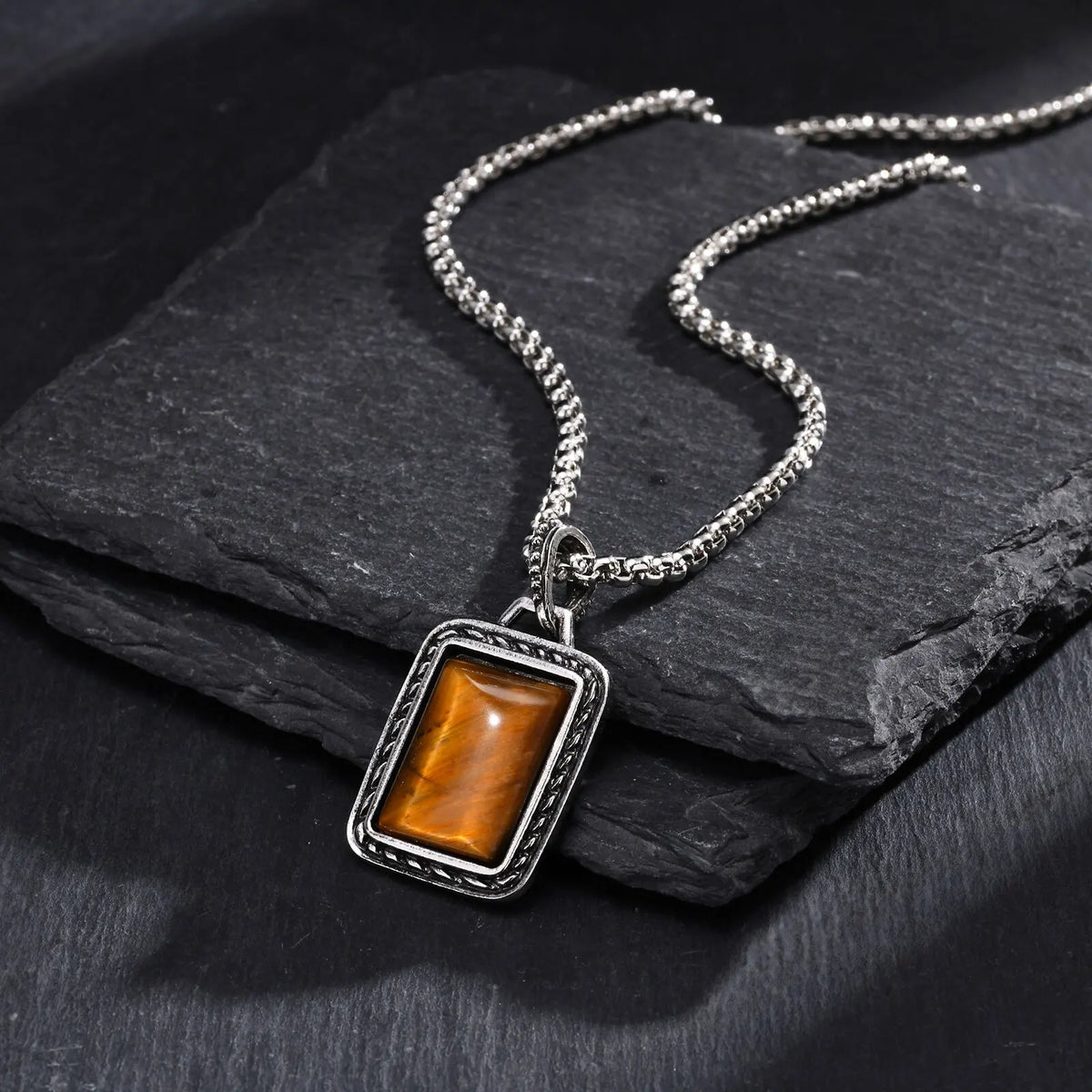 pendentif oeil de tigre homme avec monture rectangulaire argentée posé sur des plaques d’ardoise sombre