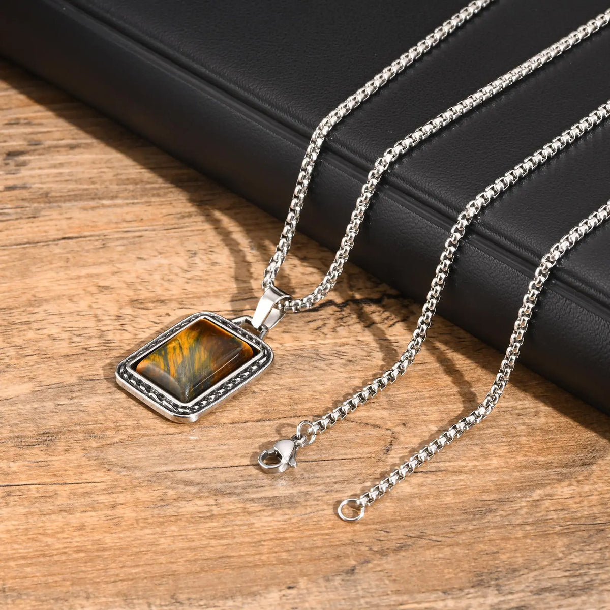 pendentif oeil de tigre homme présenté avec sa chaîne argentée et son fermoir sur une table en bois