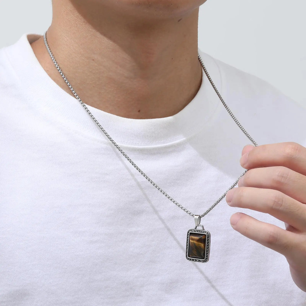 pendentif oeil de tigre homme porté sur un t-shirt blanc avec la chaîne tenue entre les doigts